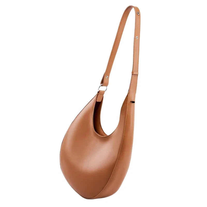 elegant brown leather bag, with a moon design and adjustable strap, hanging.