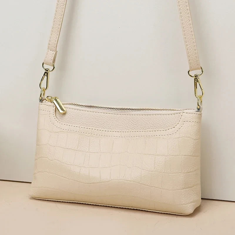 Elegant beige leather bag with crocodile texture and adjustable strap creating sophisticated and modern look.