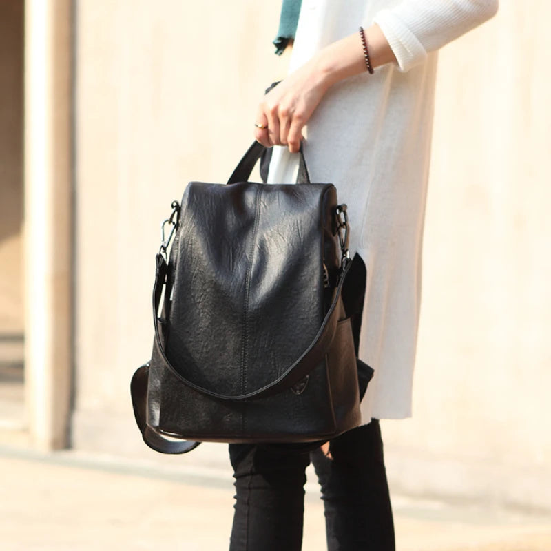 A stylish black anti-theft leather backpack carried by a woman in a casual outfit.