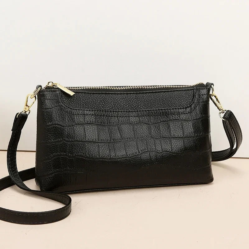 Black leather bag in crocodile texture with gold zipper - front view.