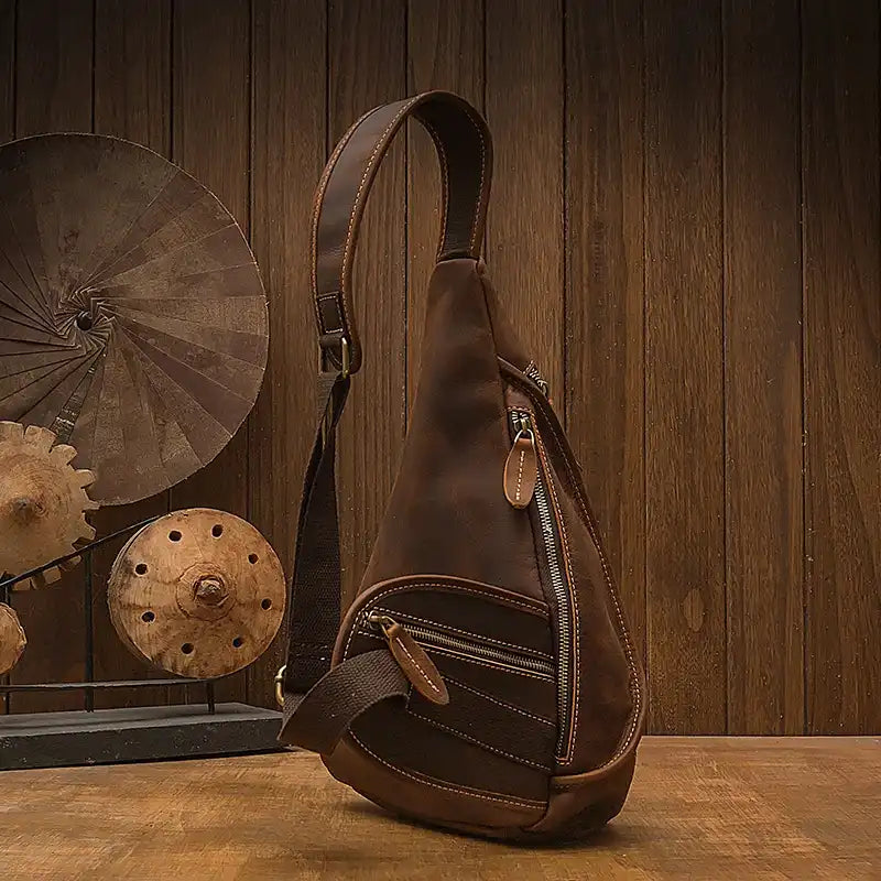 Close-up of the details on a brown leather sling bag, featuring zippers and pockets - back view.