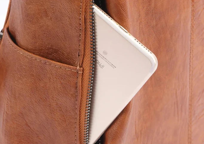Close-up of a leather bag with a smartphone partially visible in the zipper pocket.