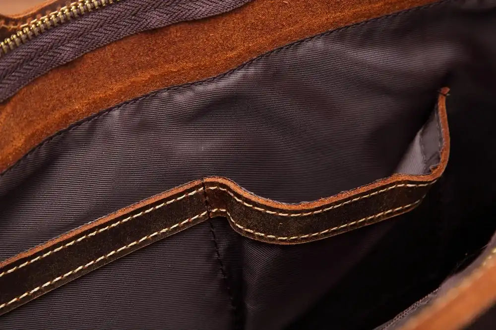 Inside of a brown leather bag, showing the main compartment and a smaller pocket, highlighting the stitching details.
