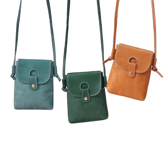 Three leather bags in different colors, blue, green and orange, hanging on a light wall.
