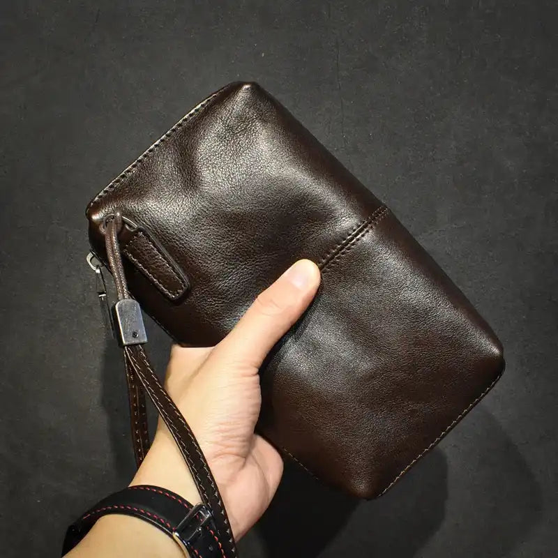 A stylish dark brown leather wallet held in hand by leather wrist strap - front view.