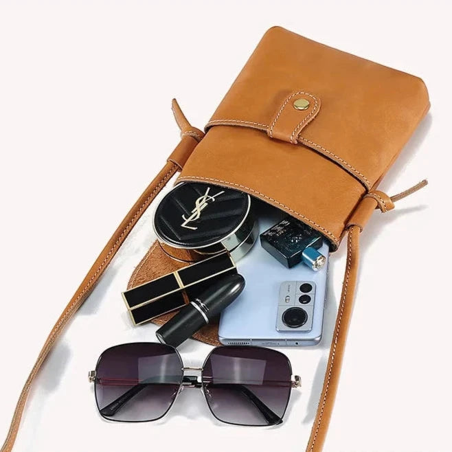 brown leather bag opens to display essentials such as makeup, sunglasses and a smartphone, perfect for everyday wear.