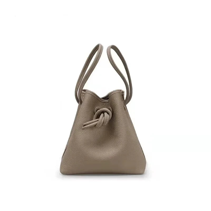 A stylish gray leather bag with a unique knot design and dual handles - front view.