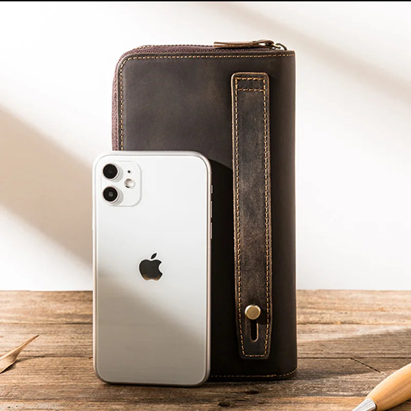 A stylish leather wallet beside a phone on a wooden surface for size reference.