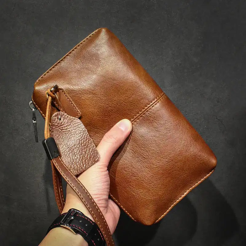 A stylish brown leather wallet held in hand by leather wrist strap - front view.