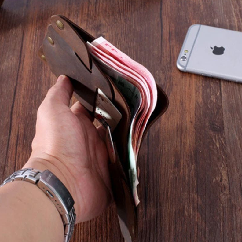 A man holding a brown leather wallet full of money and cards, on a wooden table.
