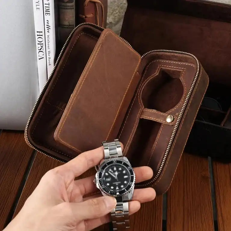 A hand holding a stylish watch next to a brown leather watch case.