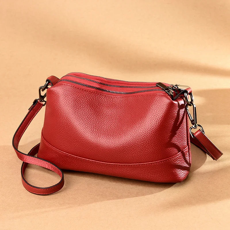 A stylish red leather shoulder bag, featuring three zippered compartments and an adjustable strap, front view.
