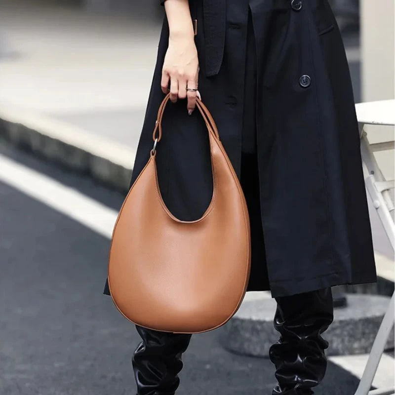 model holding an elegant brown leather bag, with a moon design and adjustable strap.