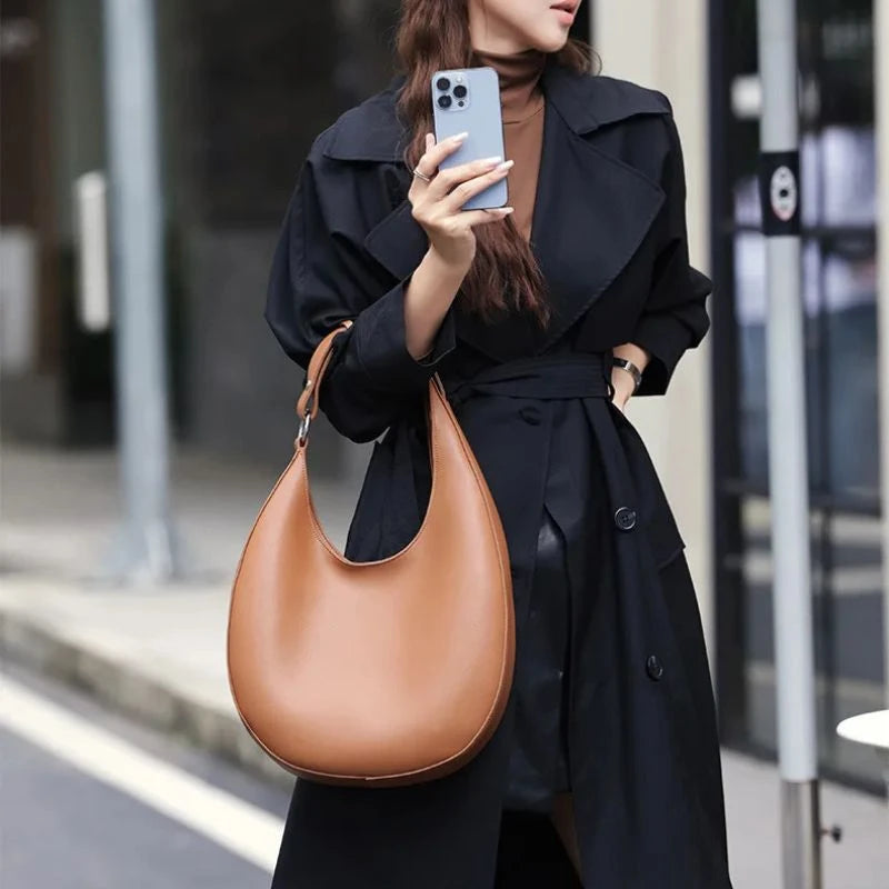 woman in black coat holding an elegant brown leather bag, with a moon design and adjustable strap 