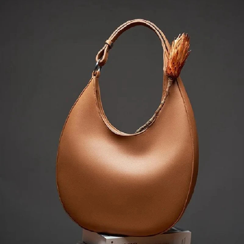Display of an elegant brown leather bag, with a moon design and adjustable strap, front view.