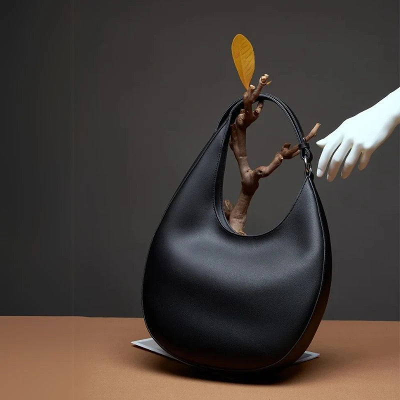 Elegant black oval leather bag with a branch and leaf detail.