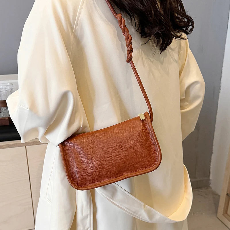 A stylish brown leather crossbody bag with a braided strap worn over the shoulder.