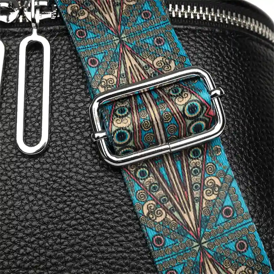Detail of a bag strap with a colorful print and metal buckle on a black leather bag.