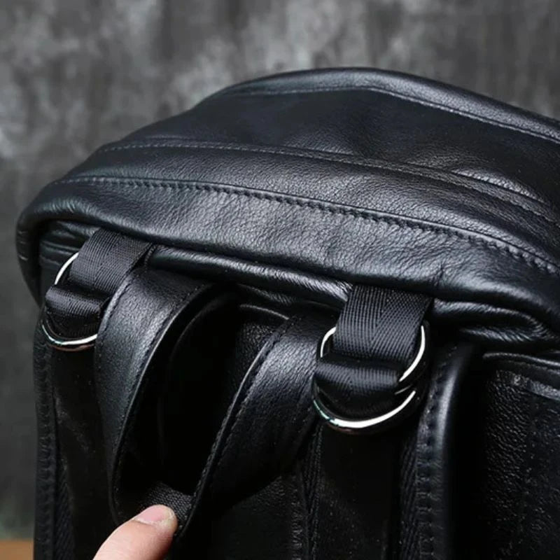 Detail of a black leather bag, showing the clasps and backpack straps and soft handle.