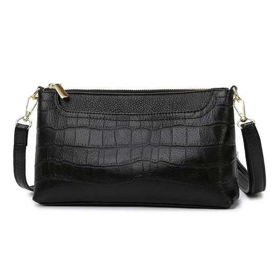 Black leather bag with crocodile texture, with removable strap and zipper closure - front view.