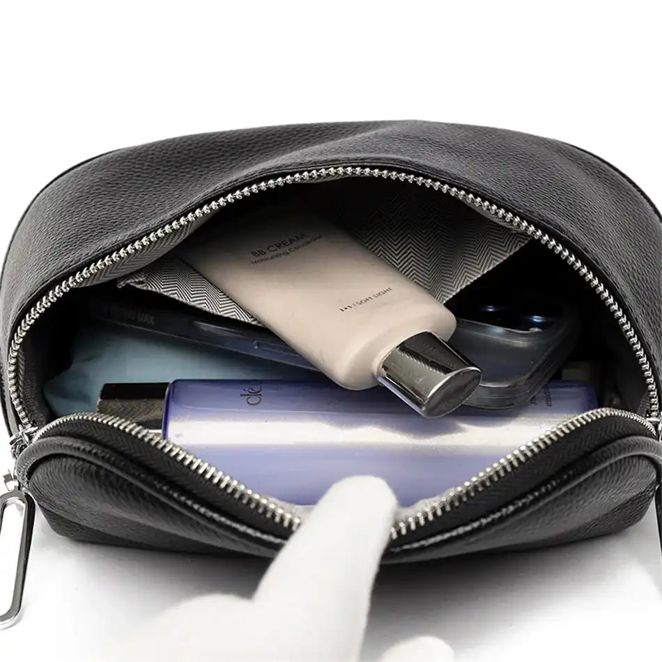 An open black leather bag displaying various beauty products and phone showcasing its large capacity.