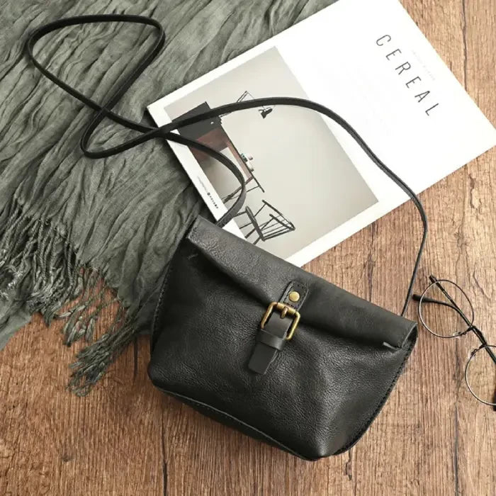 Black leather crossbody bag with elegant buckle and long strap, top view.