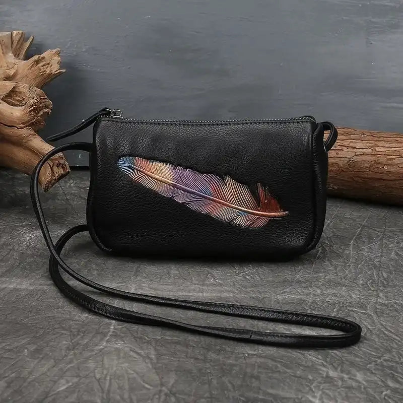Black leather crossbody bag with colorful feather embossed detail, front view.