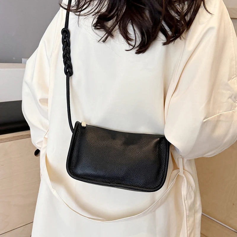A stylish black leather crossbody bag with braided strap worn over a light-colored outfit.