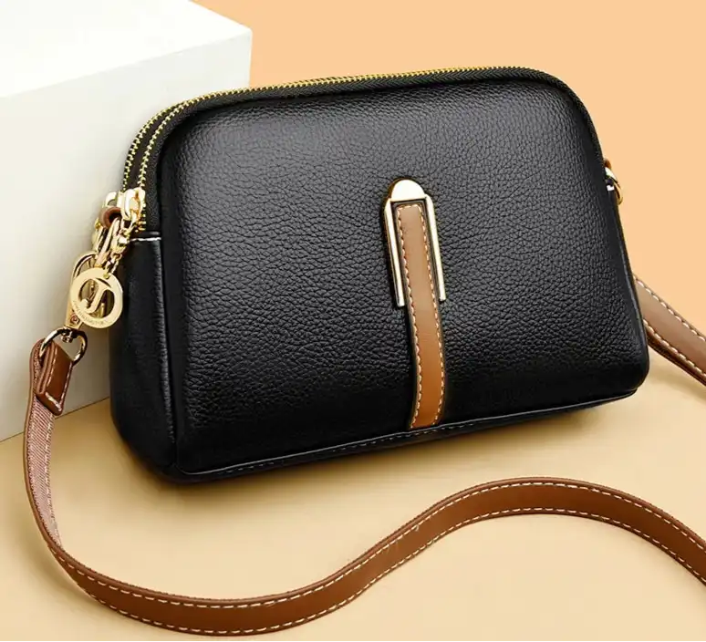 Elegant black leather crossbody bag with a brown strap and golden zipper.
