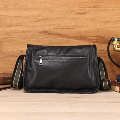 Black leather messenger bag with adjustable strap and back zipped pocket, back view.