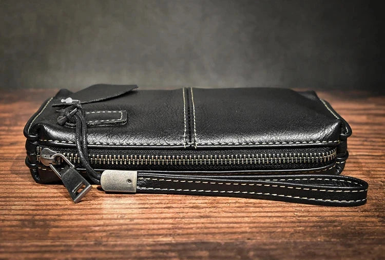 Side view of a stylish black leather wallet with a zipper and wrist strap.
