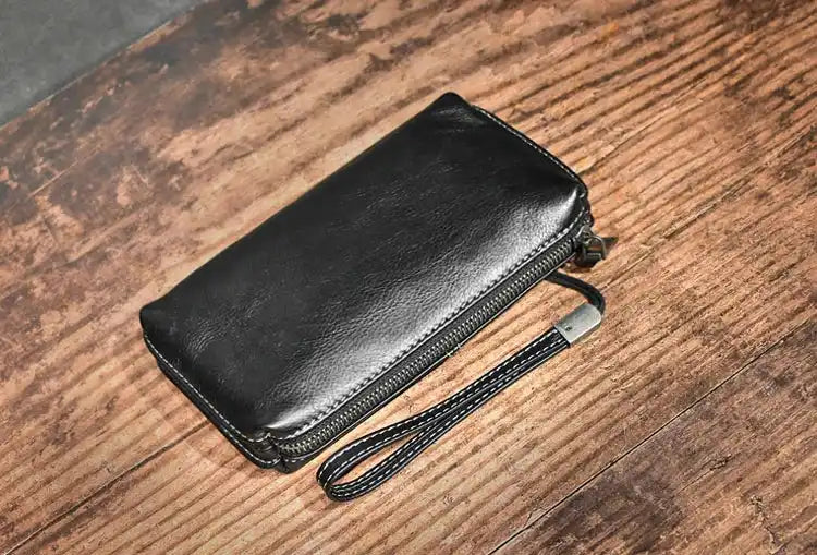A sleek black leather wallet with a zipper and wrist strap on a wooden surface.