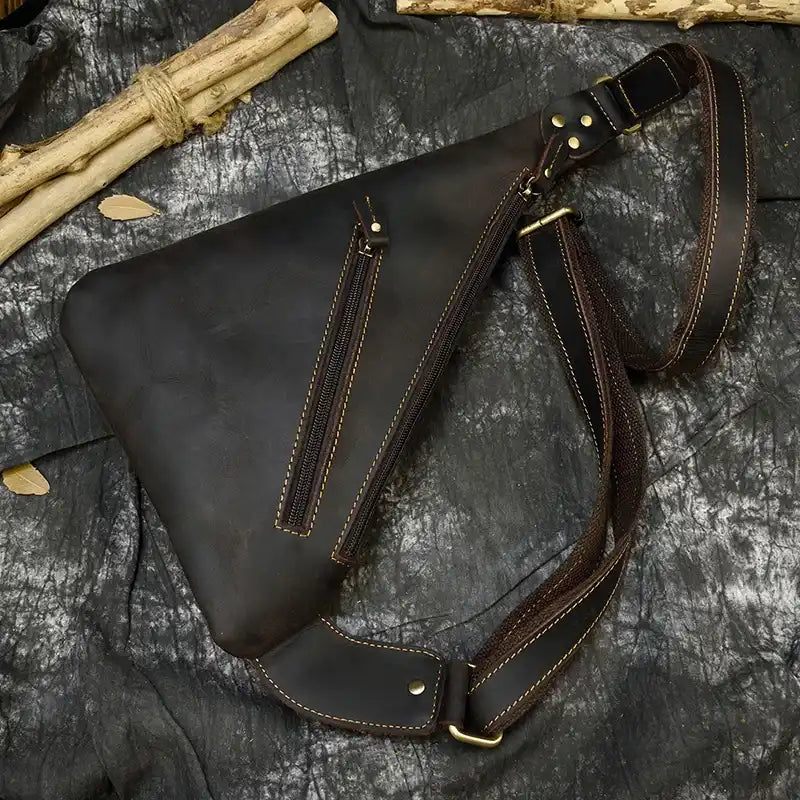 Close-up view of a black leather sling bag highlighting its zippers and strap details.
