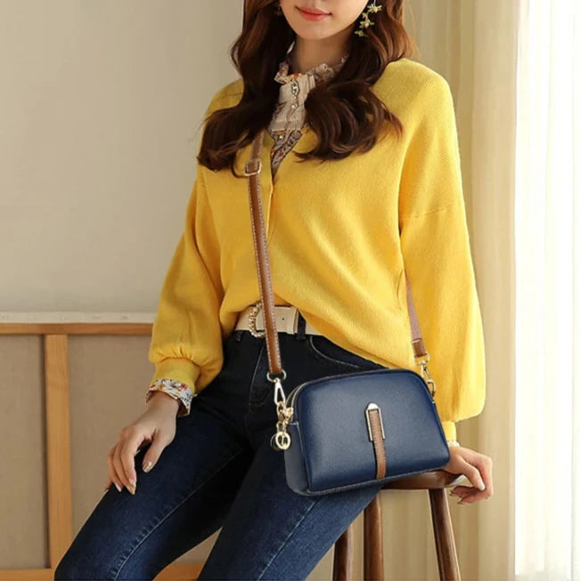 A woman wearing a stylish blue leather crossbody bag, sitting indoors.