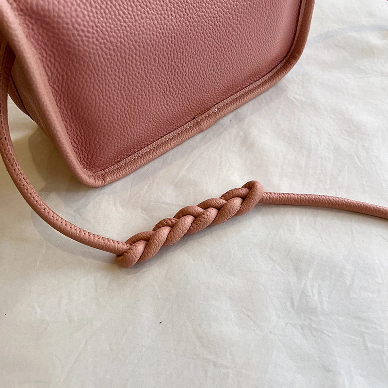 close-up view of a stylish pink leather bag with a braided strap.