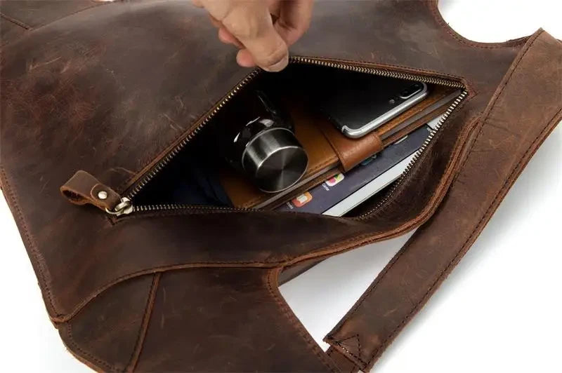 Brown leather bag with zipper, showing an interior filled with items such as a cell phone, notebook and bottle.