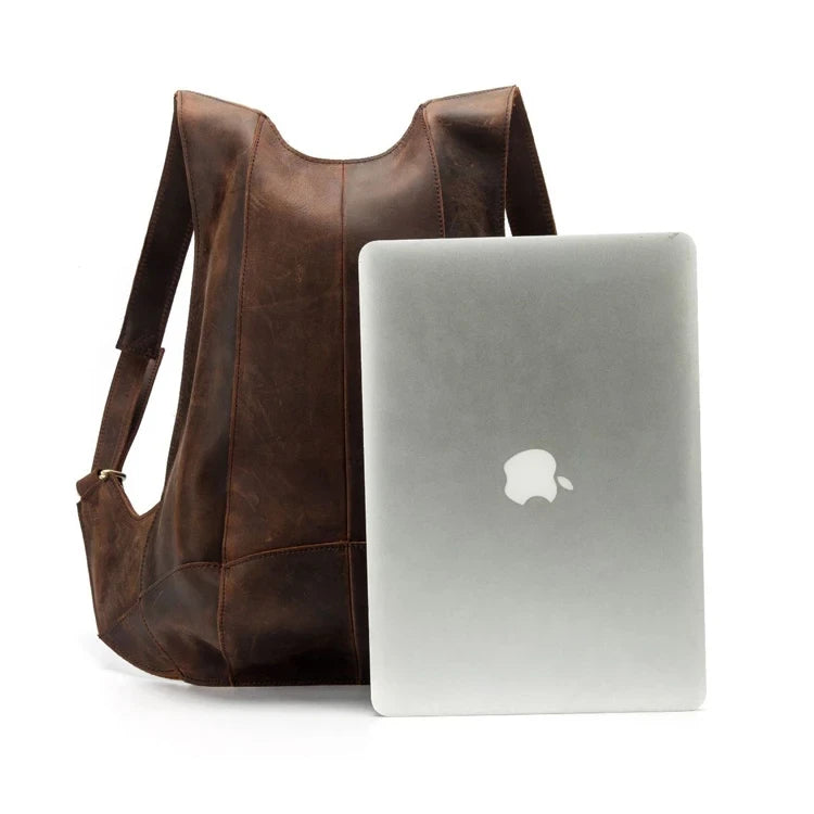 Stylish brown leather backpack next to an Apple laptop for size reference, front view.