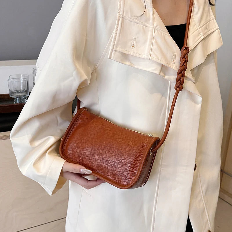 A close-up of a chic brown leather crossboby worn across the body by a woman in a white jacket.