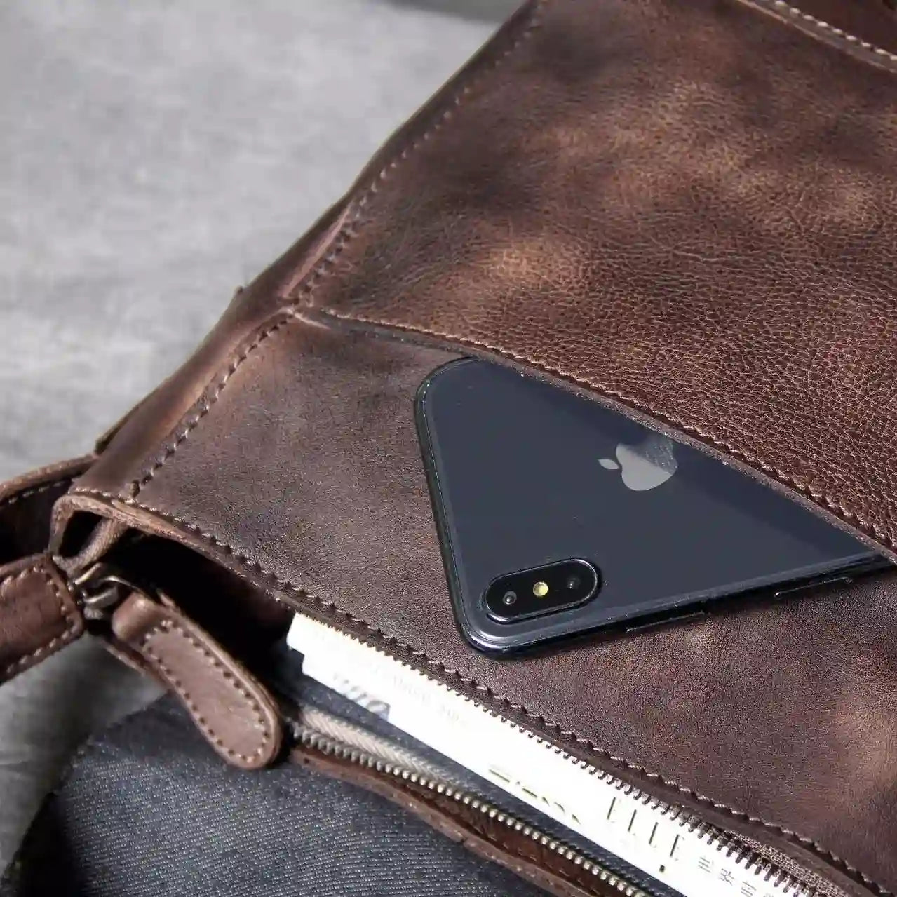 A black cell phone in a brown leather bag, showing the large storage capacity and modern style of the bag.