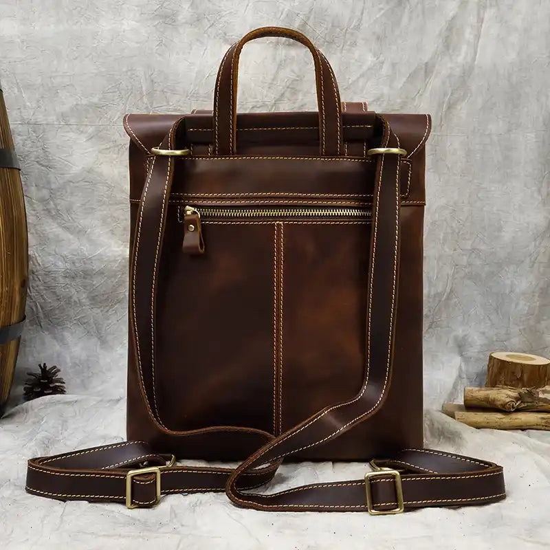 back view of an elegant brown leather bag with double handles, a shoulder strap and back zipped pocket.