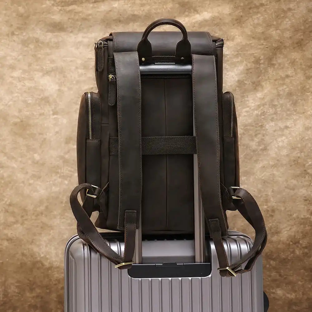 Durable brown leather backpack designed for travel, placed on top of a travel suitcase.