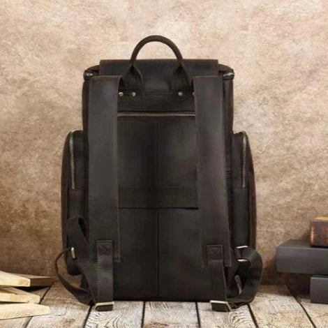 Back view of a brown leather backpack with padded straps, ideal for carrying laptops and everyday use.