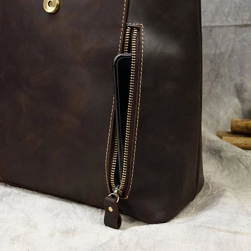 Detailed view of a brown leather bag with front zipped phone pocket with smartphone inside.