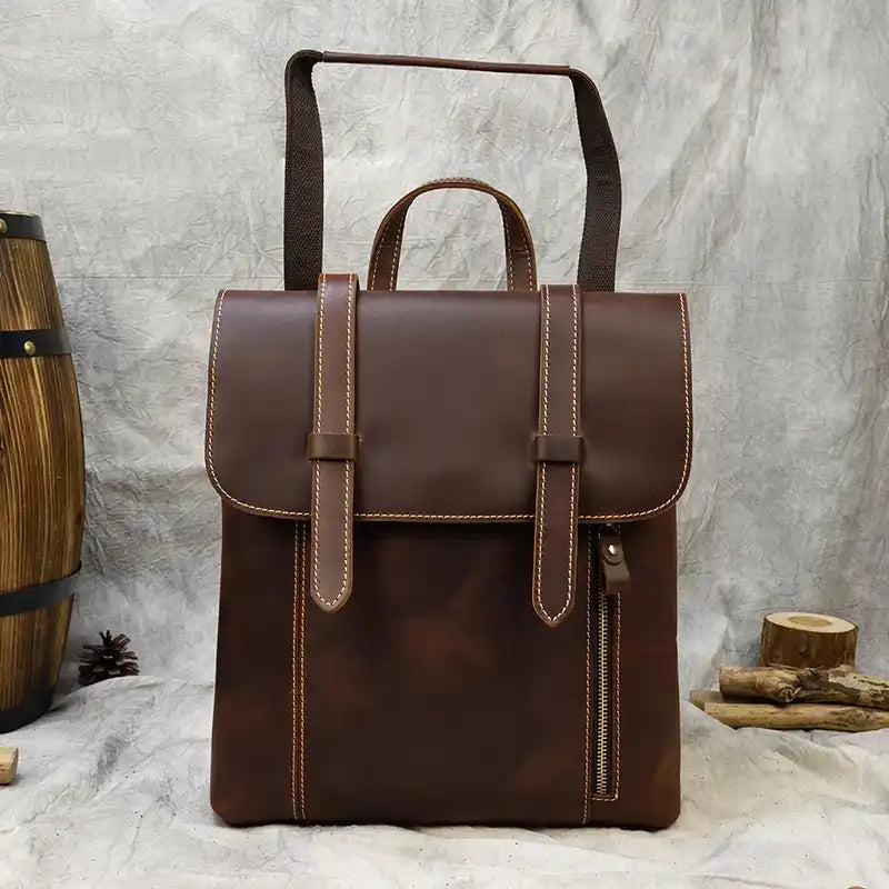 Brown leather backpack with light stitching details, front zipper, soft handle and adjustable strap, front view.