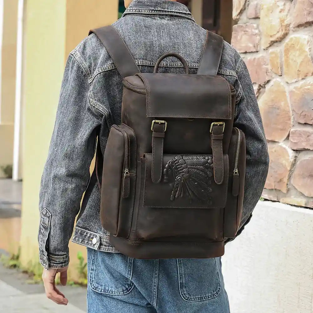A man in a denim jacket presents a brown leather backpack with embossed details.