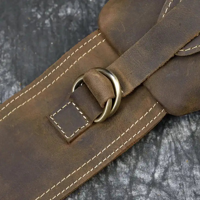 Detail of a brown leather belt with a metallic buckle, showing contrasting stitching.