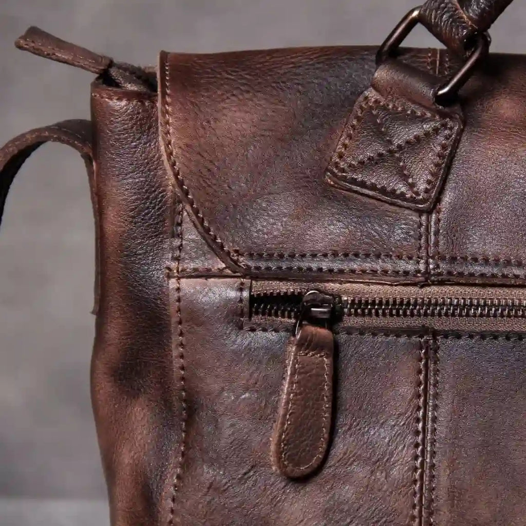 Detail of a brown leather bag, highlighting its zippers and fine stitching details.