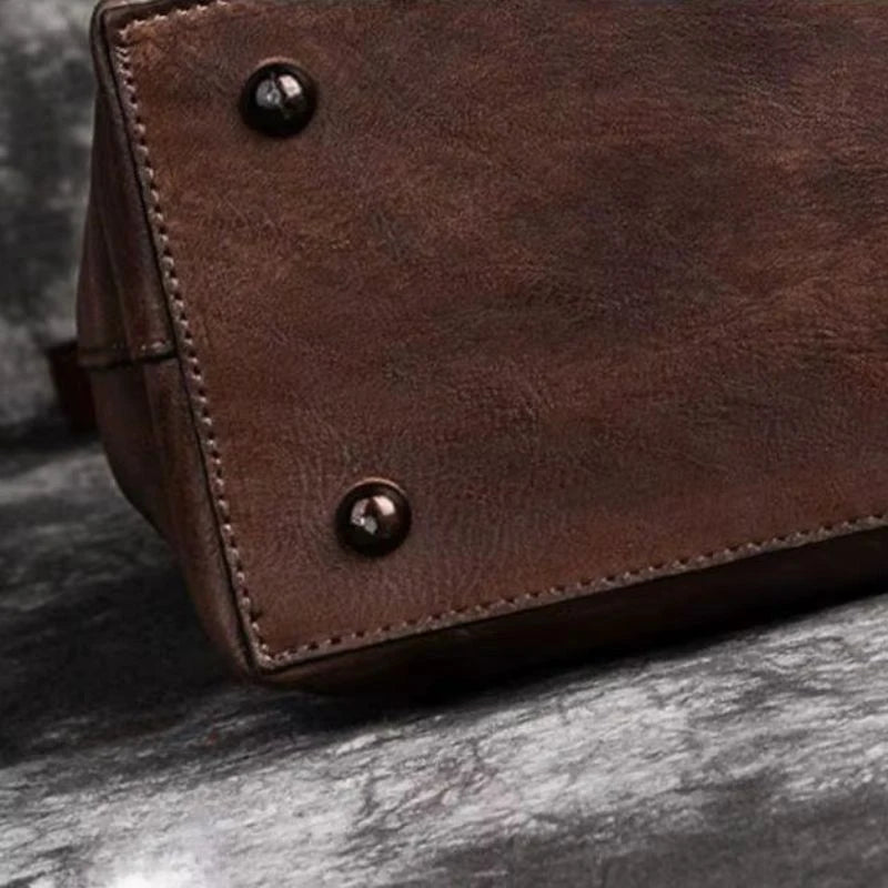 Close-up image of a brown leather bag, highlighting its finishing, stitching and metal buttons, bottom view.