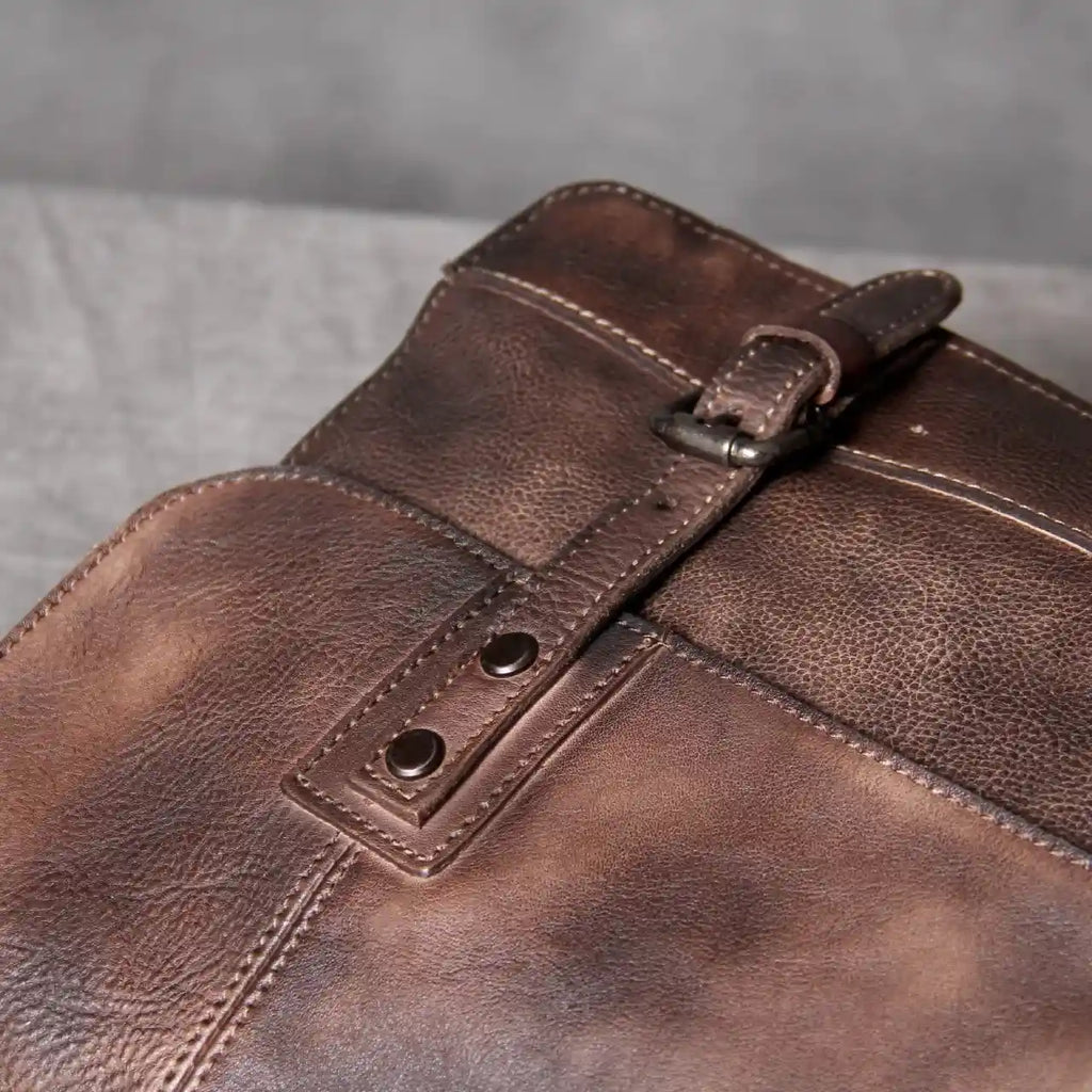 Detail of a brown leather backpack, showing the textured finish and buckle closure.