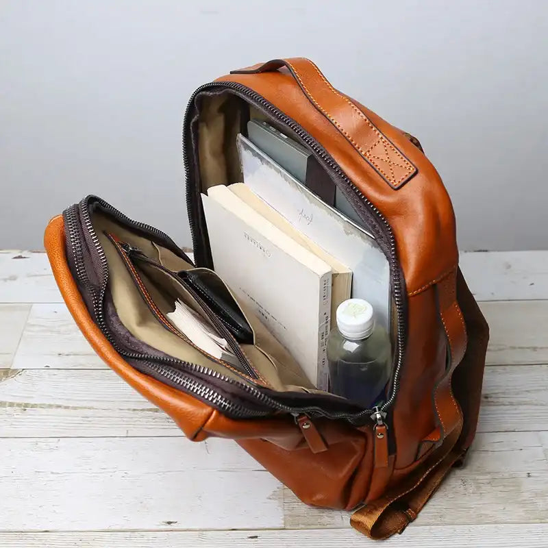 open brown leather backpack showing notebooks, books and a bottle of water inside.